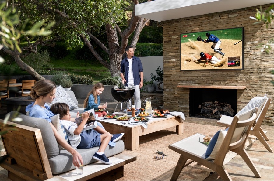 A family is gathered around on an outdoor patio with a TV installed above the fireplace in a Tarrant County home. 